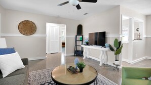 Ein Wohnzimmer mit Deckenventilator, einem runden Couchtisch mit Dekoration, einem Fernseher und einem grünen Sessel.