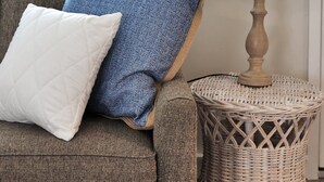 Ein braunes Sofa mit zwei Kissen, ein Korbstuhl als Beistelltisch und eine weiße Lampe.