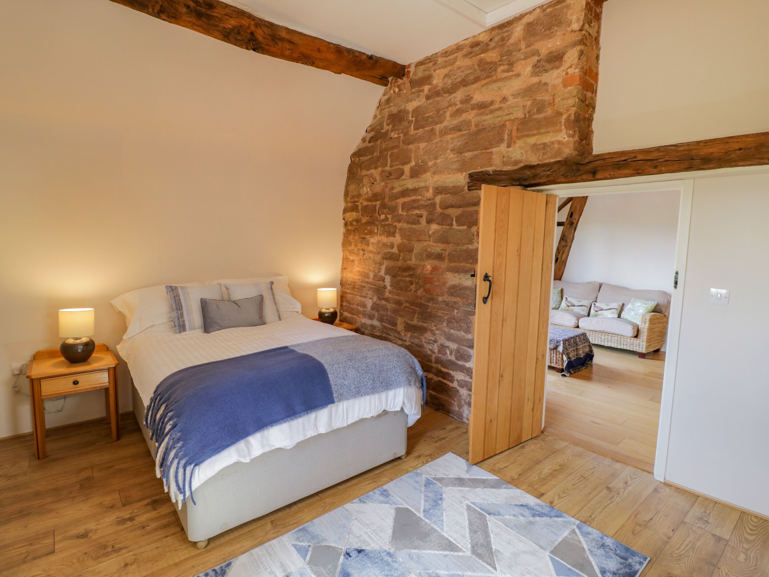 Une chambre à coucher avec un lit, des tables de chevet en bois, un mur en briques et une porte en bois donnant sur une autre pièce.