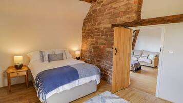 Une chambre à coucher avec un lit, des tables de chevet en bois, un mur en briques et une porte en bois donnant sur une autre pièce.