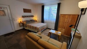 Un dormitorio acogedor con cama, lámparas de noche, un armario de madera, una mesita y una ventana con cortinas.