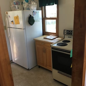 A compact kitchen with a refrigerator, stove, and wooden cabinets.