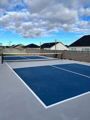 An outdoor tennis court with a net, surrounded by a fence, and houses in the background. - Full pickleball court, kings beds, HUGE clean home (Enoch)