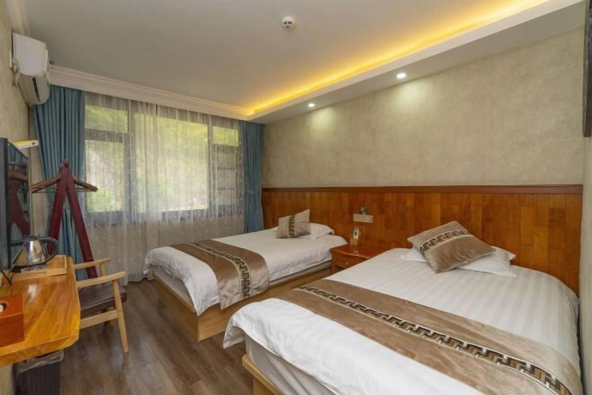 Ein Hotelzimmer mit zwei Betten, einem Holztisch, einem Stuhl und einem Fenster mit Vorhängen.