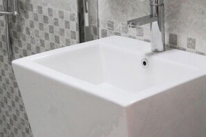 Un baño con lavamanos blanco, zona de ducha y paredes de azulejos.