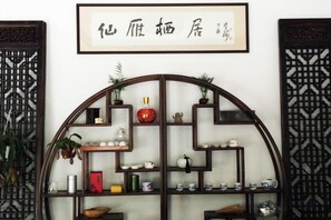 Une étagère de style chinois traditionnel, ornée de divers objets décoratifs, et au-dessus de laquelle est accrochée une œuvre calligraphique encadrée.