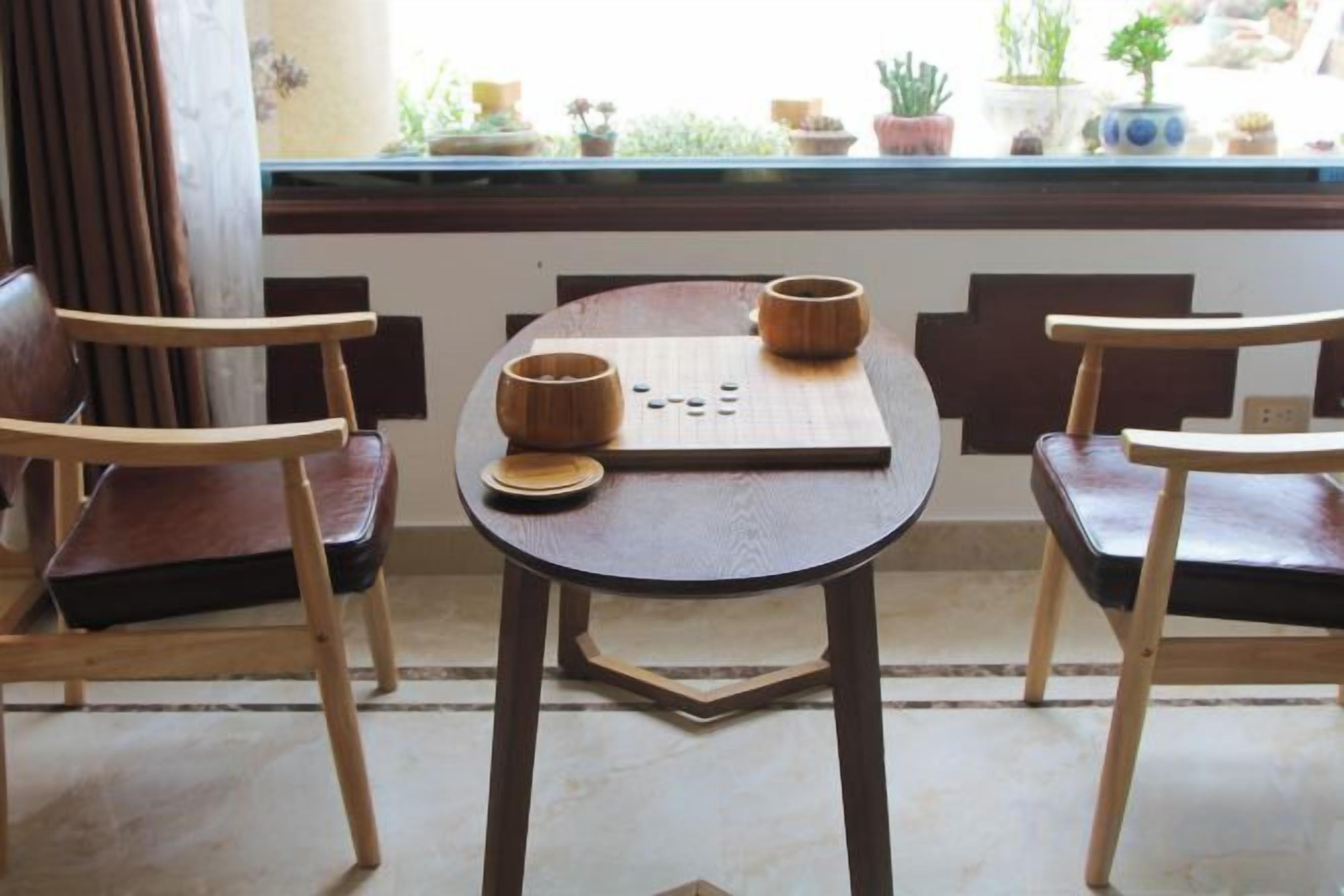 A wooden table with two chairs, a board game, and a window with plants.