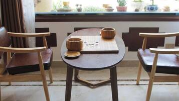 A wooden table with two chairs, a board game, and a window with plants.