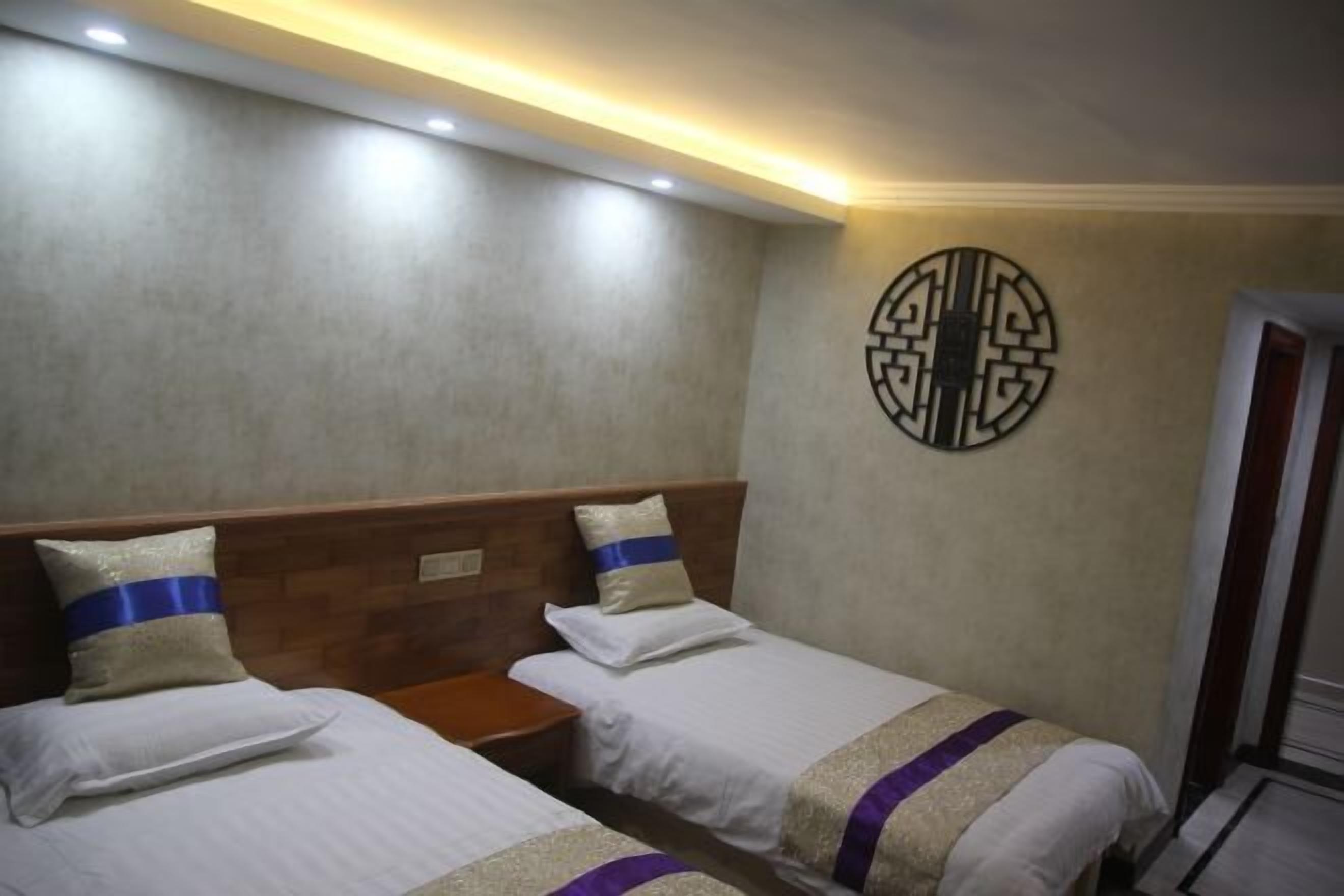 Habitación de hotel con dos camas, cabecera de madera, un adorno en la pared y una puerta a la derecha.