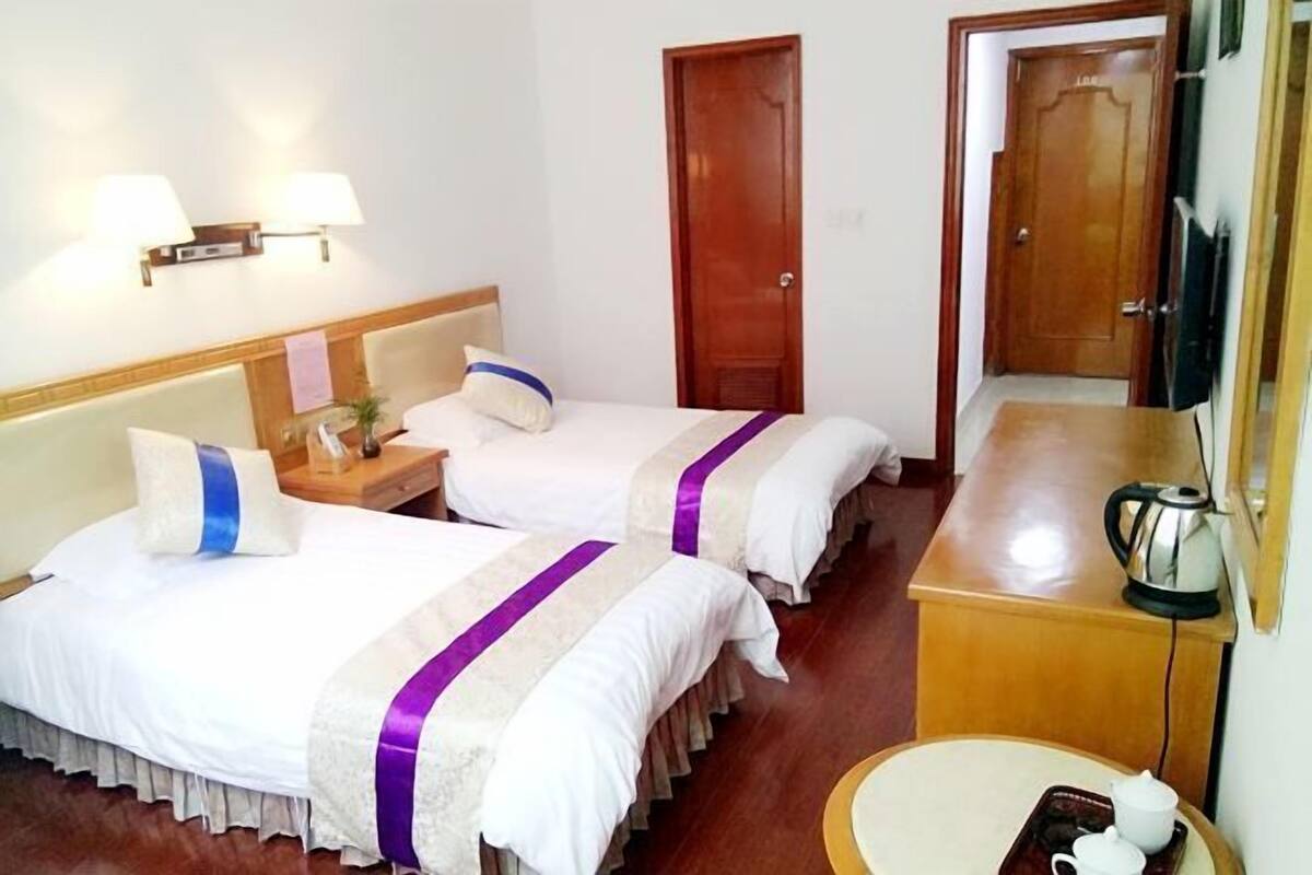 Ein Hotelzimmer mit zwei Betten, einem Holzkopfende, einem Nachttisch mit Lampe, einem Spiegel und einem kleinen Tisch mit Wasserkocher und Tassen.
