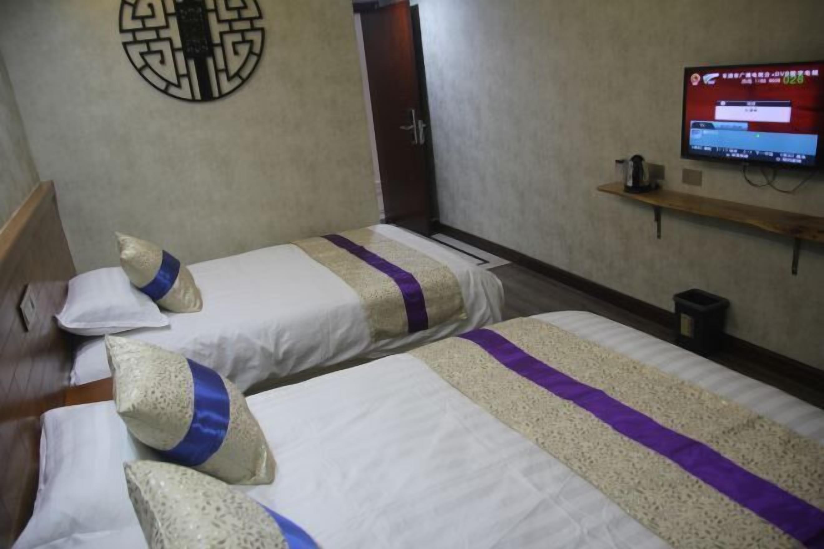 Ein Hotelzimmer mit zwei Betten, einem an der Wand befestigten Fernseher und einem kleinen Hocker mit einem Wasserkocher.