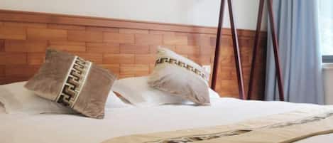A bed with a wooden headboard, two pillows with a geometric pattern, and a hanging wooden rack.