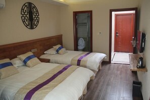 Habitación de hotel con dos camas, cabecero de madera, televisor montado en la pared y puerta que da a un baño.