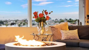 A cozy living room with a view of a cityscape, a table with a vase of flowers, and a lit fire.