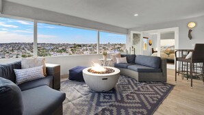 A modern living room with a large window, a fire pit, and a view of the city.