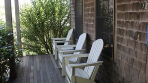 Un portico in legno con tre poltrone Adirondack e un edificio in mattoni con una finestra.