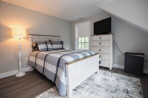 A bedroom with a bed, bedside lamp, dresser, TV, and a window. - Mid Island Townhouse (Nantucket)