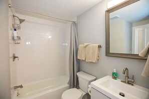 A bathroom with a bathtub, toilet, sink, and a shower curtain. - Mid Island Townhouse (Nantucket)