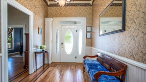 Un pasillo con un banco de madera, una puerta blanca con un panel de vidrio y un espejo en la pared.