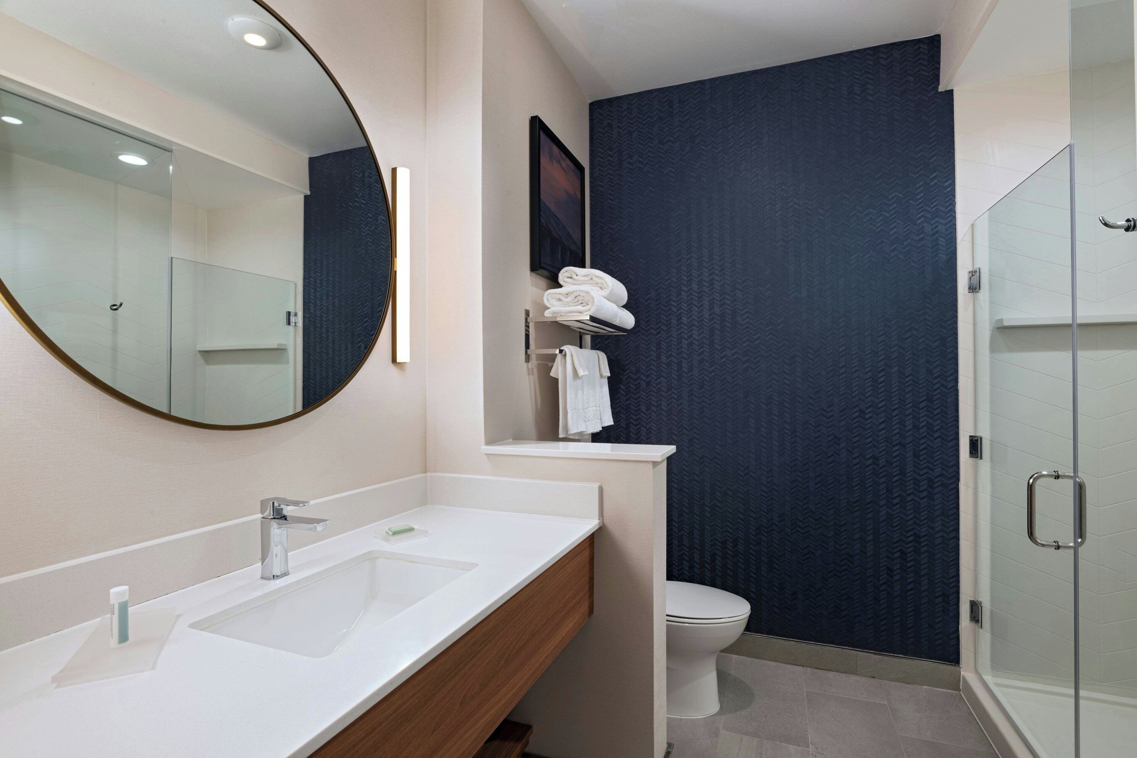 A modern bathroom with a large mirror, a sink, a toilet, and a shower area.