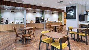 A modern restaurant with wooden tables and chairs, a kitchen area, and a motivational quote on the wall. - Fairfield Inn & Suites by Marriott Fort Worth Alliance Airport (Fort Worth)