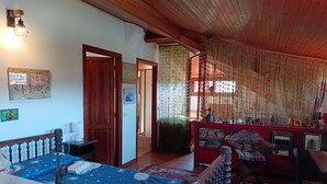 A room with a bed, a desk, a chair, and a red sofa. There is a wooden ceiling and a wall with a picture.