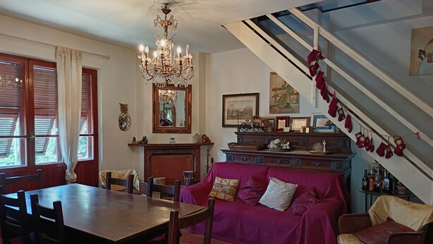A dining area with a wooden table and chairs, a purple sofa, a chandelier, and a staircase with red mittens.
