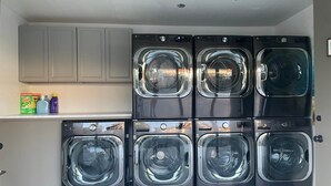 Une buanderie équipée de six machines à laver à chargement frontal superposées, d’une étagère contenant des produits de nettoyage et d’un meuble gris placé au-dessus.