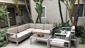 Un patio extérieur moderne avec un canapé d’angle beige, une table basse en verre et des chaises en métal blanc.