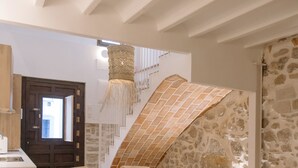 A cozy dining area with a round table and chairs, a stone wall, and a staircase with a patterned rug.