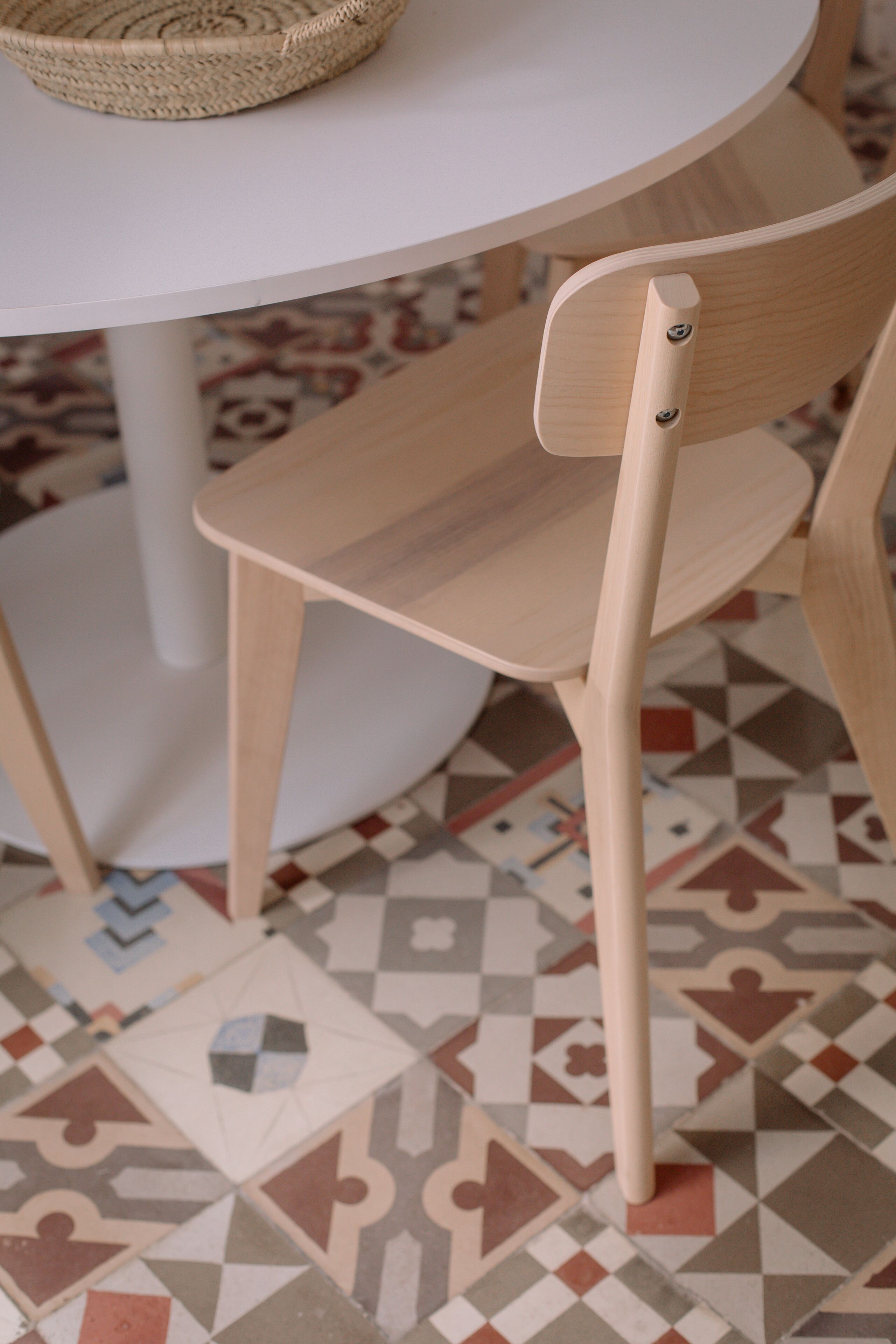 A wooden chair with a high backrest and a woven basket on a white table.
