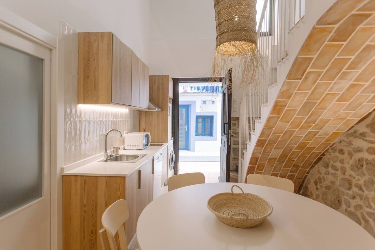 Une cuisine compacte avec des meubles en bois, un plan de travail blanc et un coin repas comprenant une table ronde et des chaises.