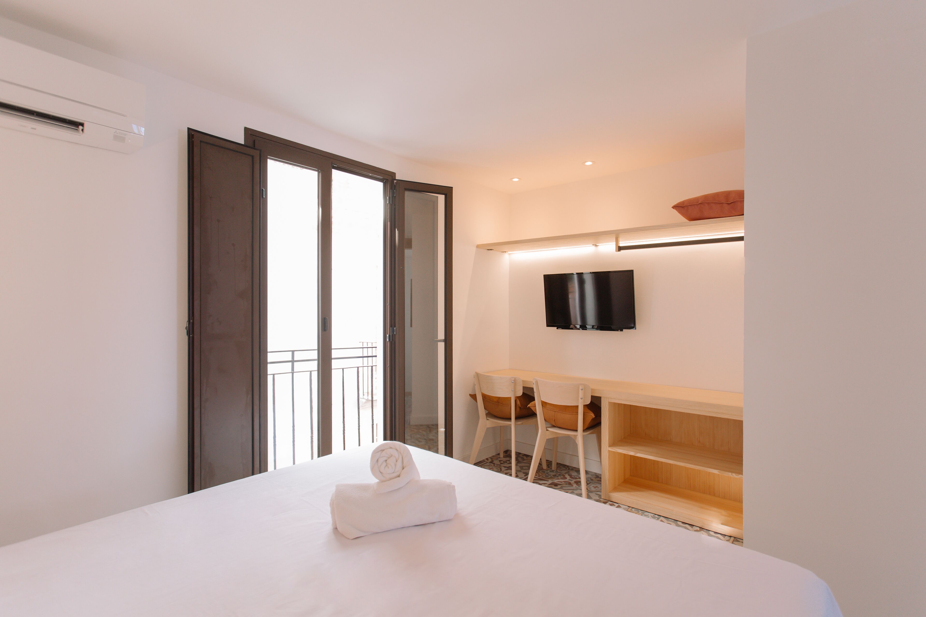 A hotel room with a bed, a desk, chairs, a TV, and a balcony.