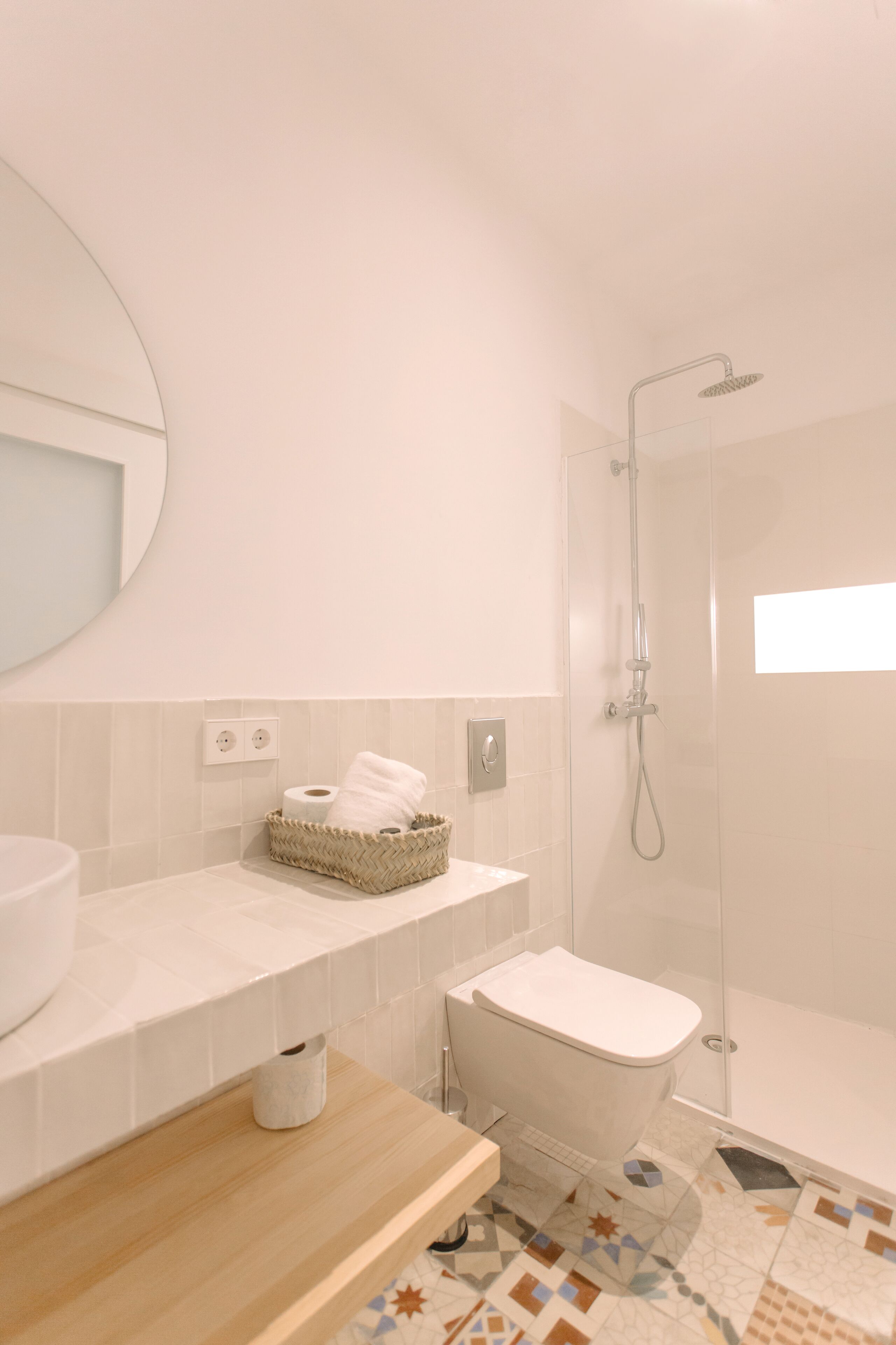 Et moderne badeværelse med toilet, bidet og bruser. Der er en træbordplade med en kurv med toiletartikler.