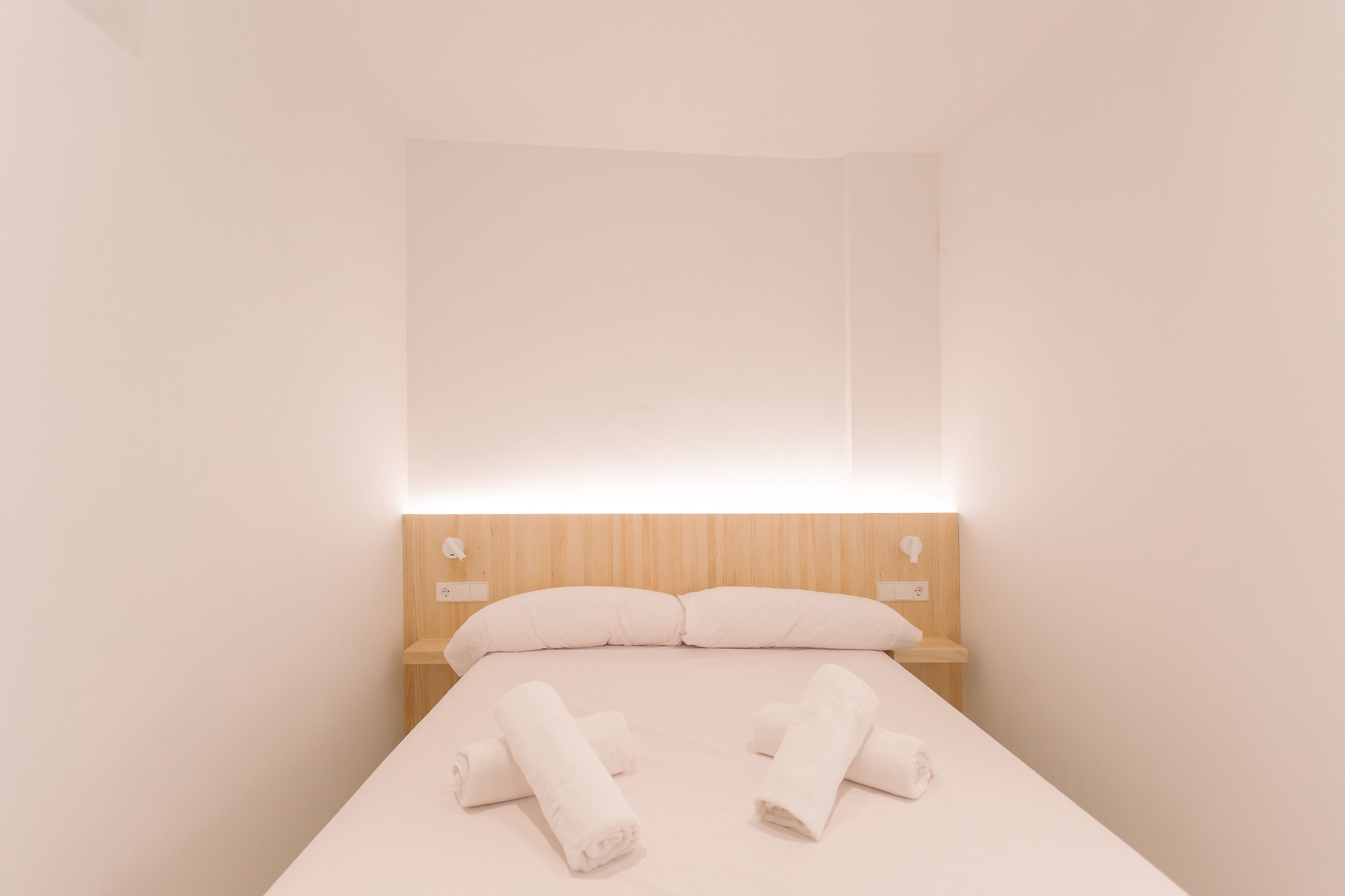 A minimalist hotel room with a bed, two pillows, and neatly folded towels.