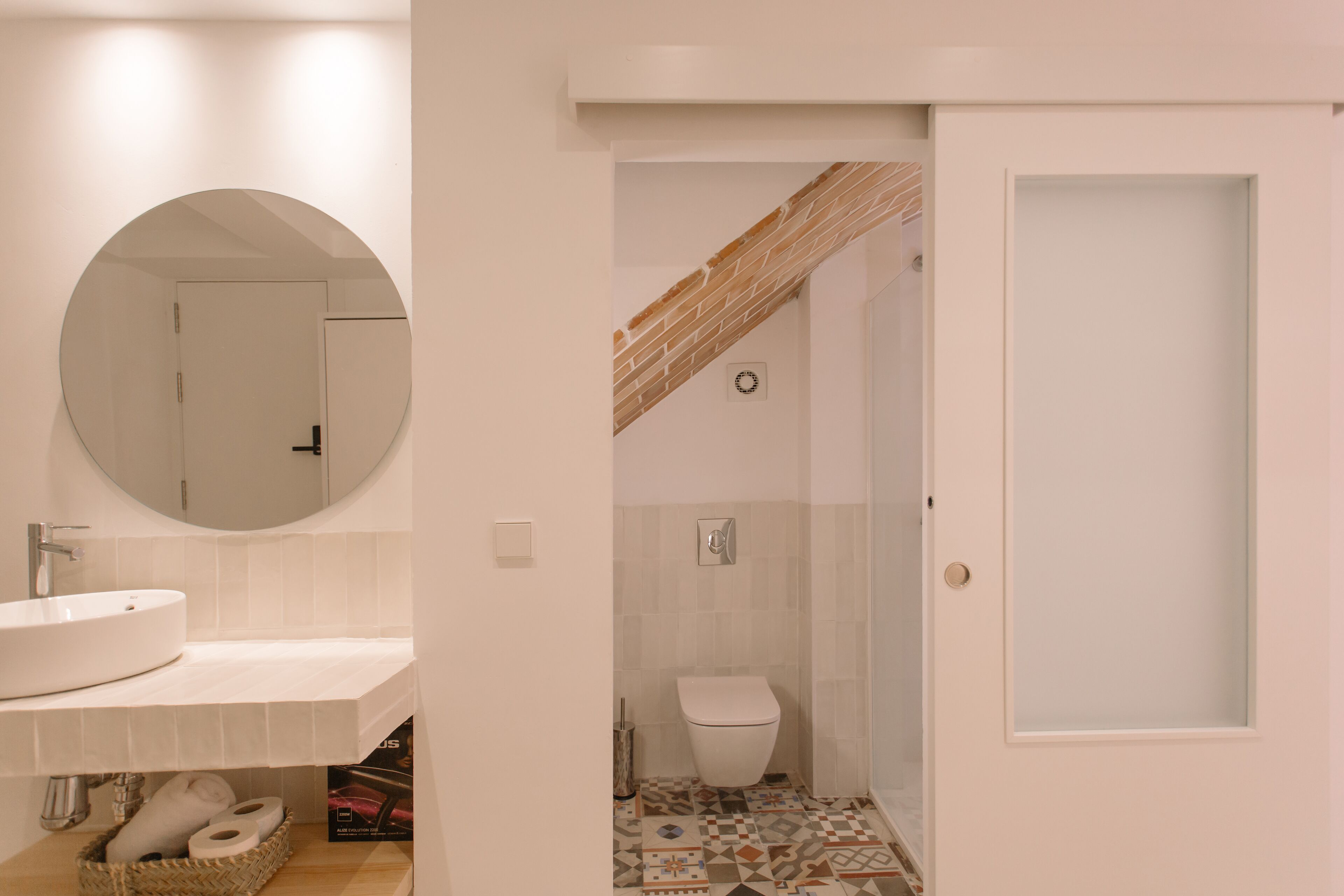 Un baño moderno con un espejo redondo, un lavabo y un inodoro.