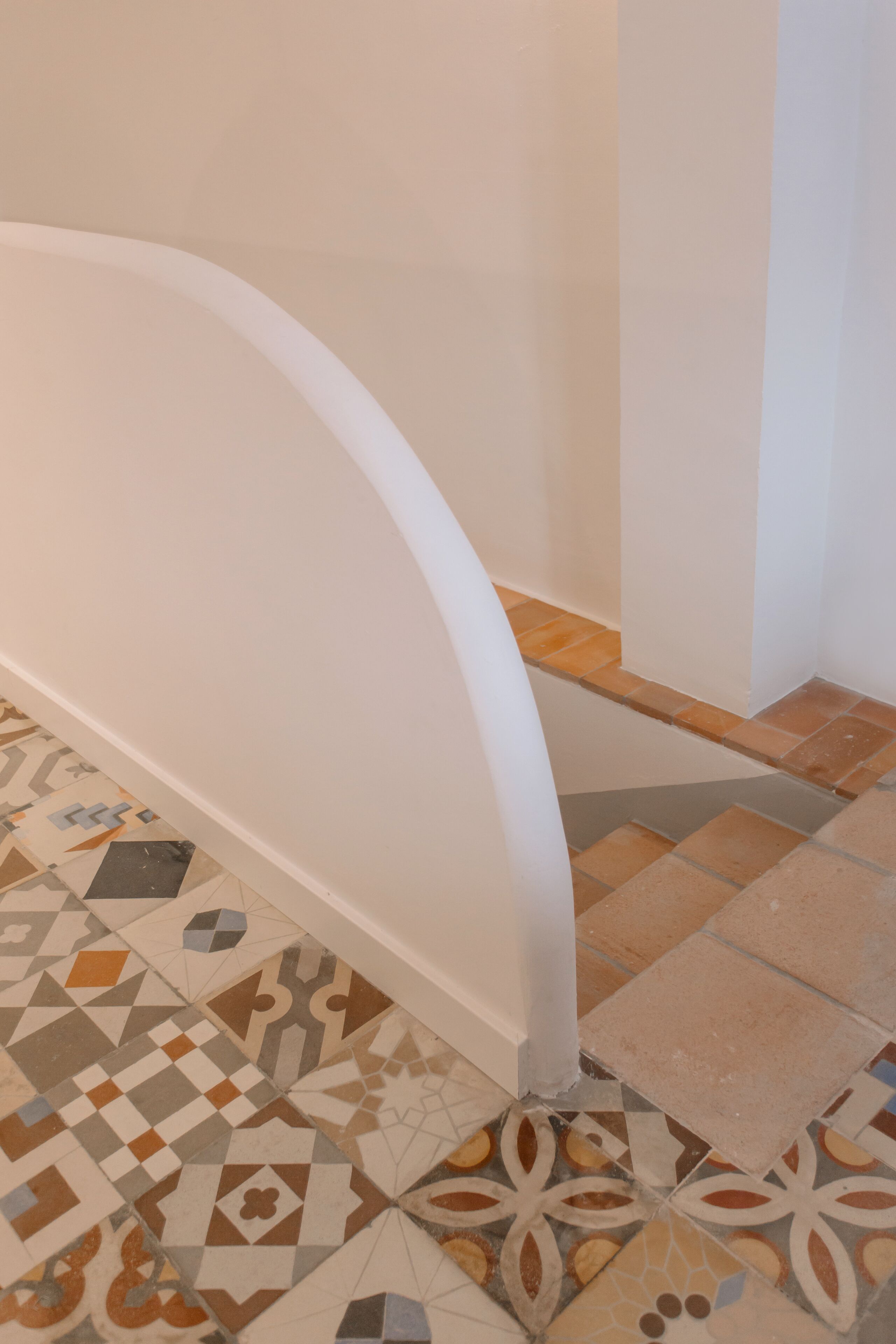 A corner of a room with a white curved wall and a patterned tile floor.