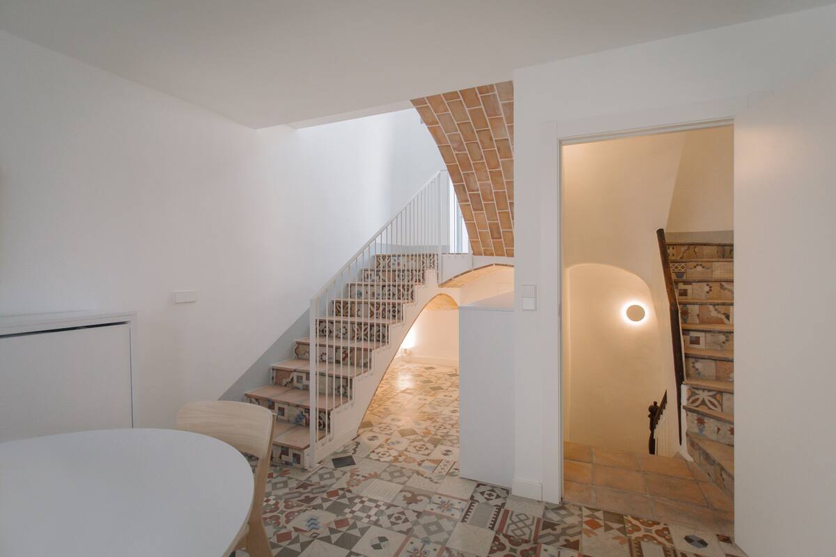Un escalier avec une rampe blanche menant à un deuxième  étage, un sol à motifs et une porte blanche dotée d’une petite fenêtre.