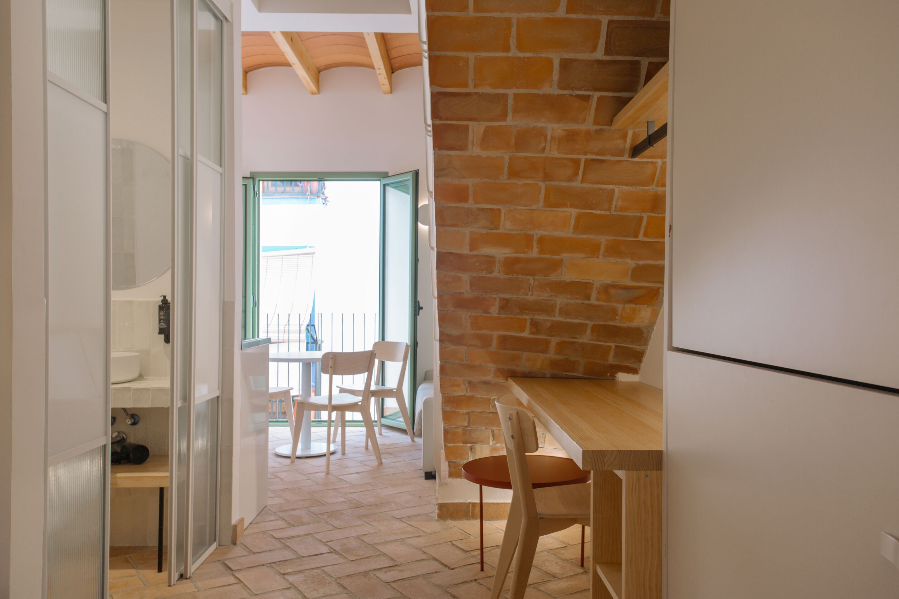 A kitchen with a brick wall, wooden counter, and a view of the outside.