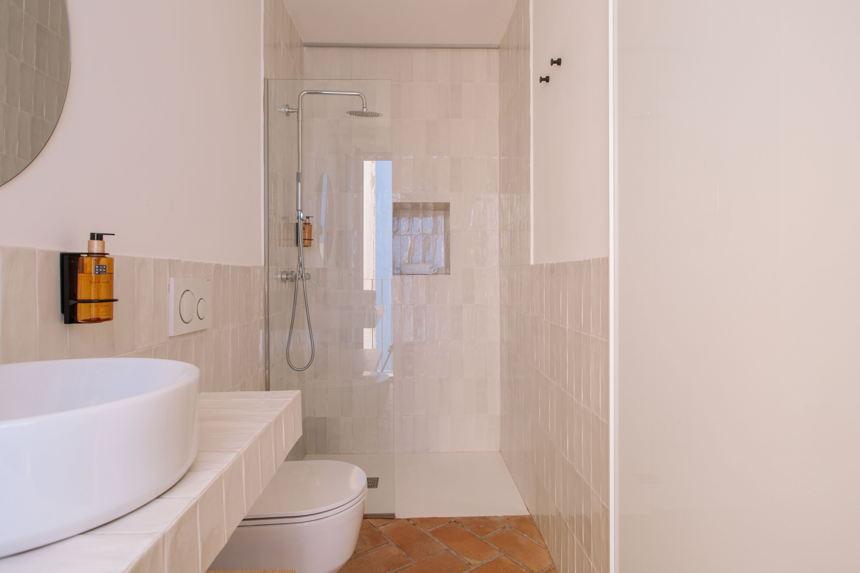 A modern bathroom with a large white bathtub, a glass-enclosed shower, and a small window.