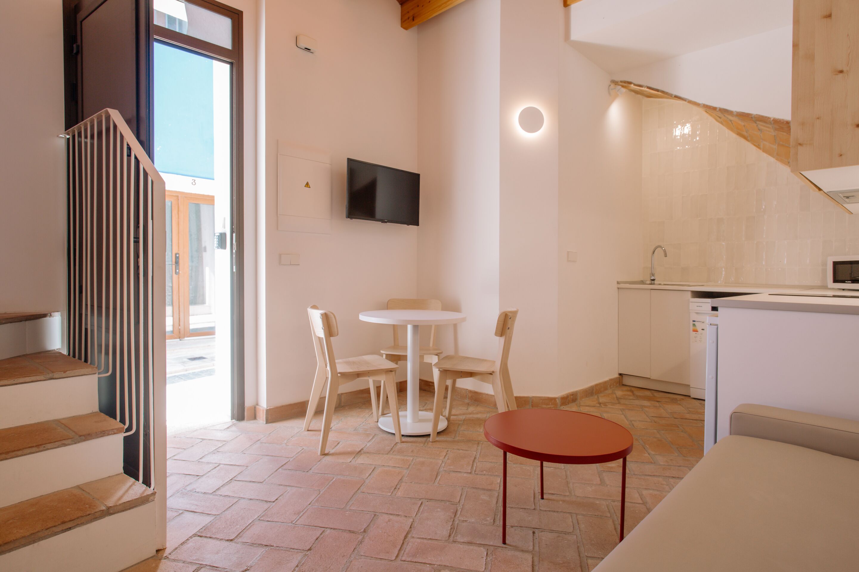 A modern kitchen with a dining area, a TV mounted on the wall, and a staircase leading to another room.