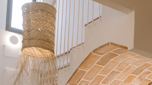 A staircase with a woven light fixture and a stone wall.