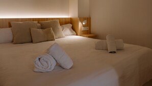 A neatly made bed with pillows and rolled towels, a bedside table with a lamp, and a circular wall light.