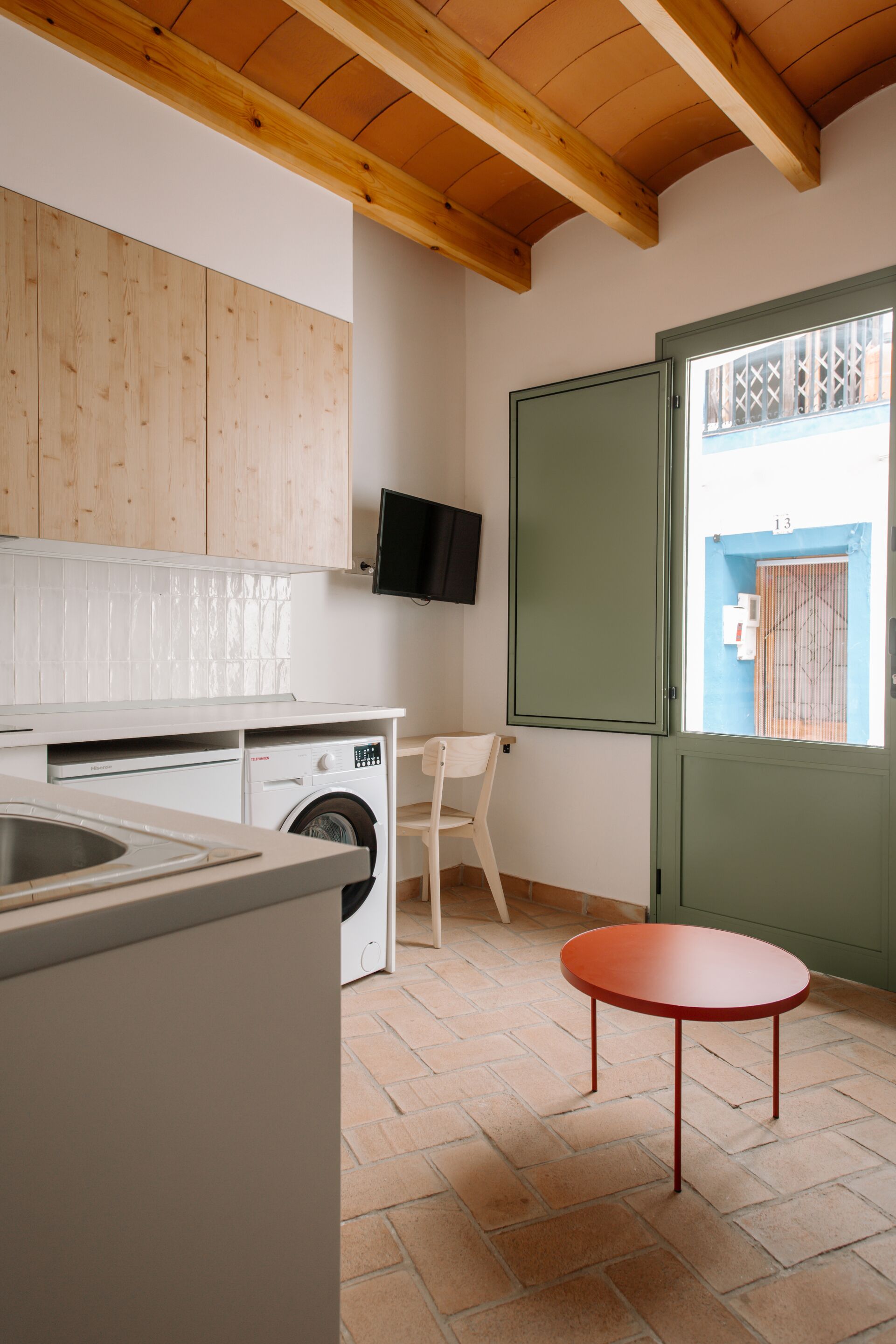 A compact kitchen with wooden cabinets, a washing machine, a small table, and a door leading to an outdoor area.