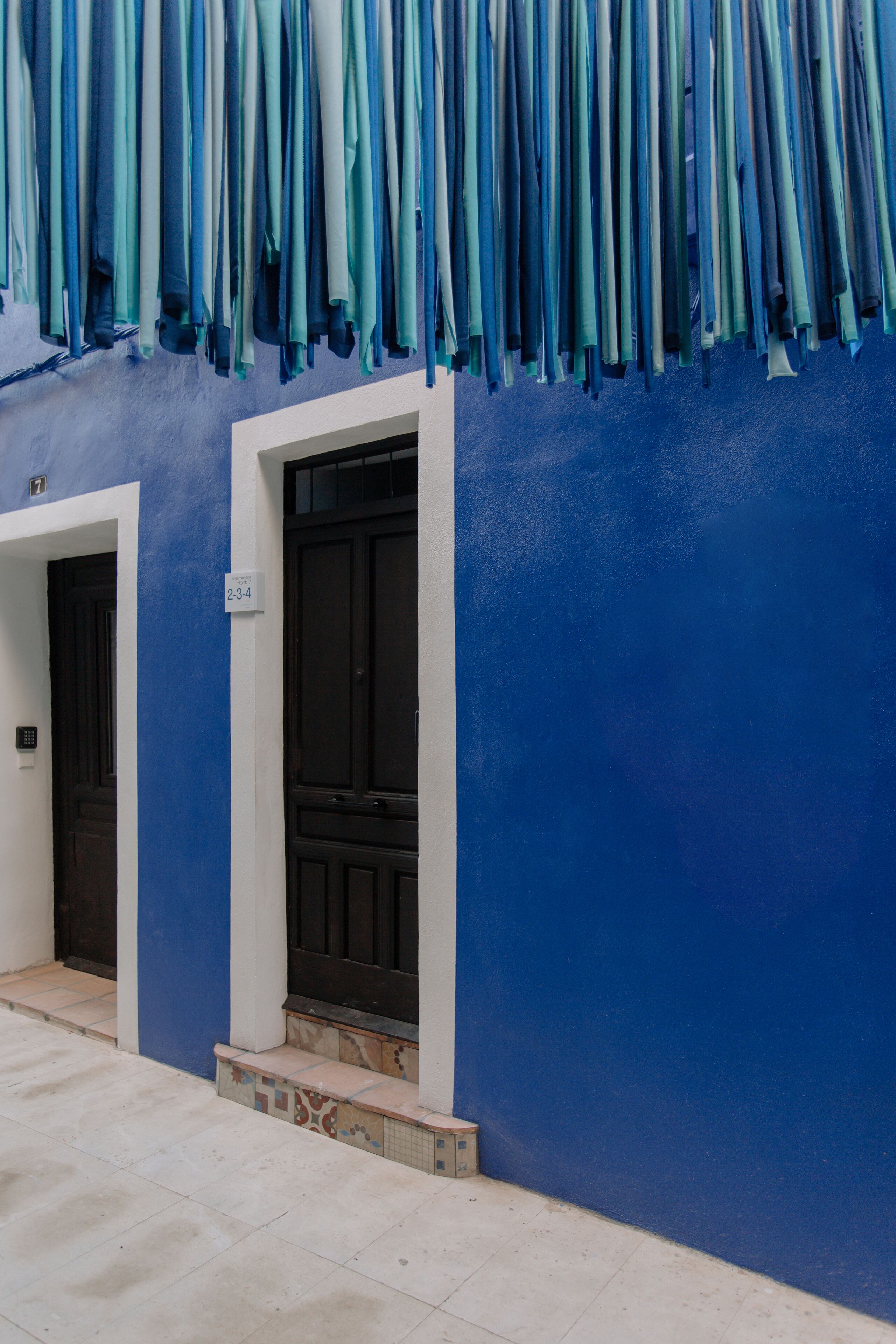 Fachada de edificio con pared azul y dos puertas negras.