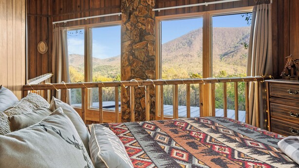 Une chambre avec un grand lit, des murs en bois, un pilier en pierre et une vue sur un paysage montagneux.