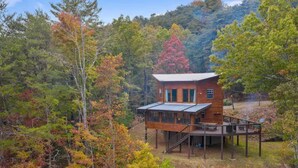Une cabane dotée d’une terrasse en bois et d’un porche abrité, entourée d’arbres aux couleurs automnales.