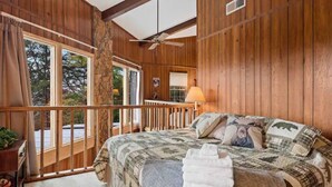 Une chambre dans une cabane en bois, avec un lit, un ventilateur de plafond et un balcon doté d’une balustrade.
