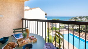 A balcony with a table set for breakfast, overlooking a pool and a coastal view. - La Gaillarde by Interhome (Les Issambres)