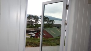 A door leading to a balcony with a view of a lake, a red building, and some greenery.